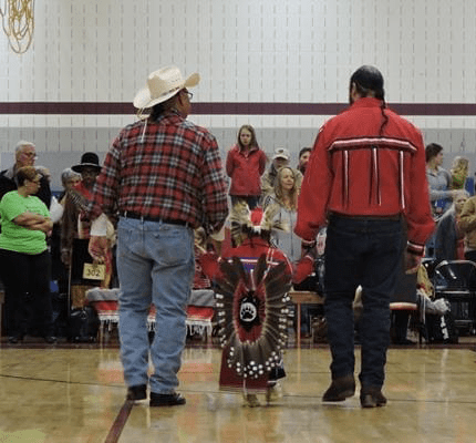 Two men holding child's hands wearing Native American clothing